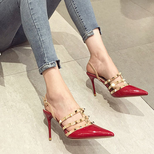Femme portant des escarpins rouges à talon aiguille avec bouts pointus et brides cloutées beiges – modèle élégant et tendance disponible chez Beloreva