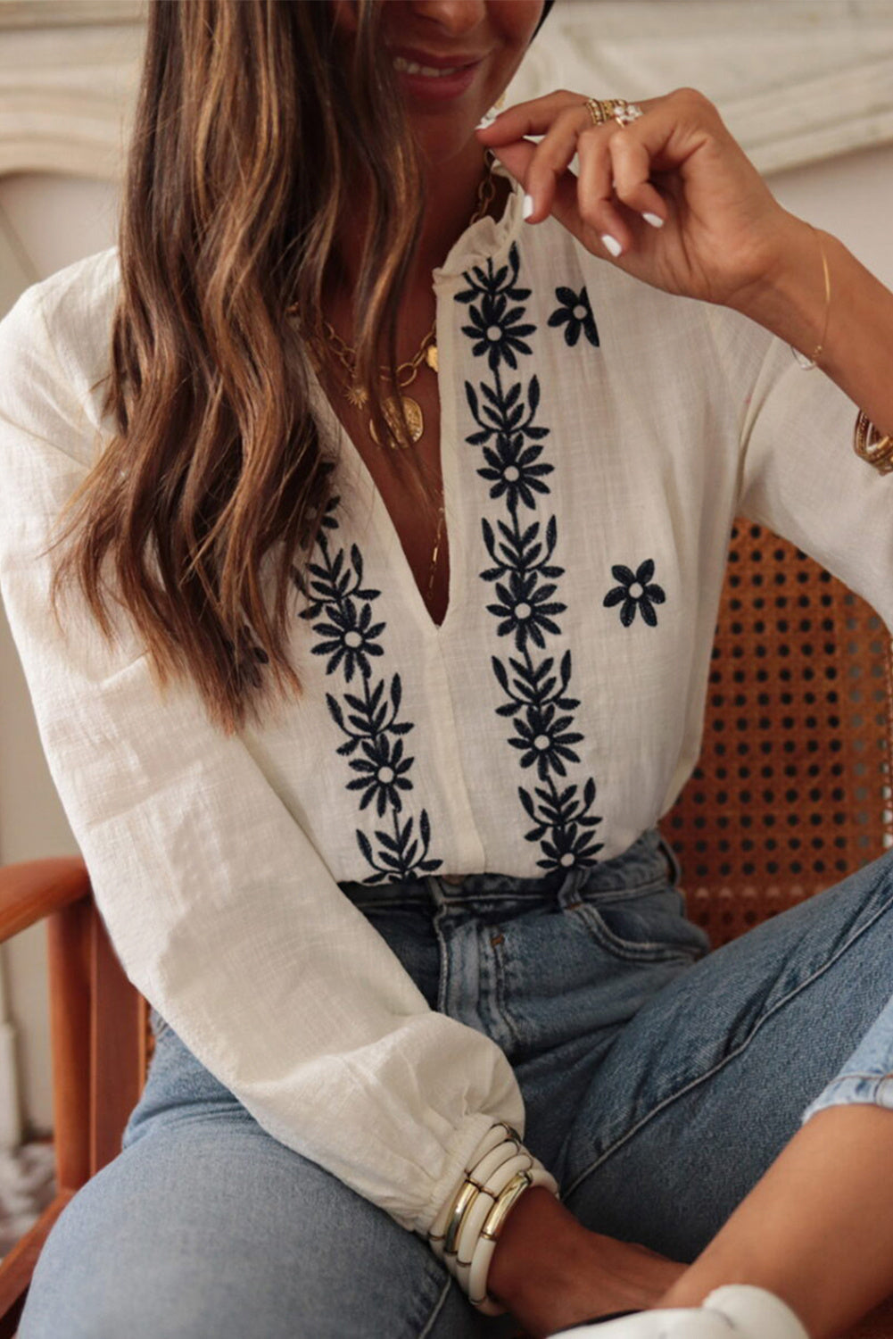 Femme portant une blouse blanche fluide avec broderies florales bleues sur le devant et manches longues – modèle bohème chic disponible chez Luxorel