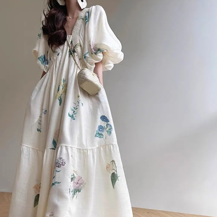 Femme portant une robe longue fluide blanche à fleurs pastel, avec manches bouffantes et coupe ample – modèle bohème et romantique disponible chez Luxorel