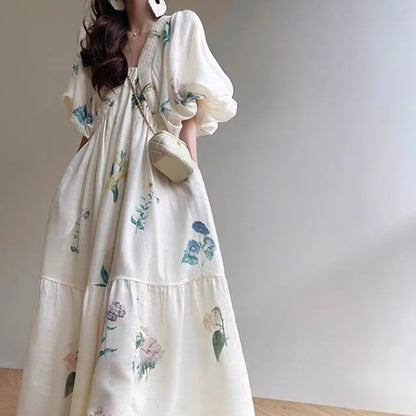Femme portant une robe longue fluide blanche à fleurs pastel, avec manches bouffantes et coupe ample – modèle bohème et romantique disponible chez Luxorel