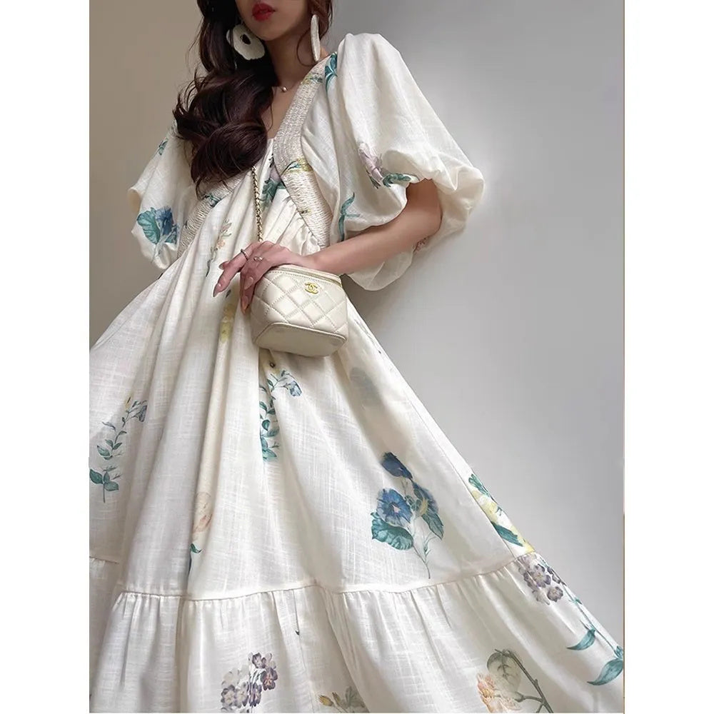 Femme portant une robe longue fluide blanche à fleurs pastel, avec manches bouffantes et coupe ample – modèle bohème et romantique disponible chez Luxorel